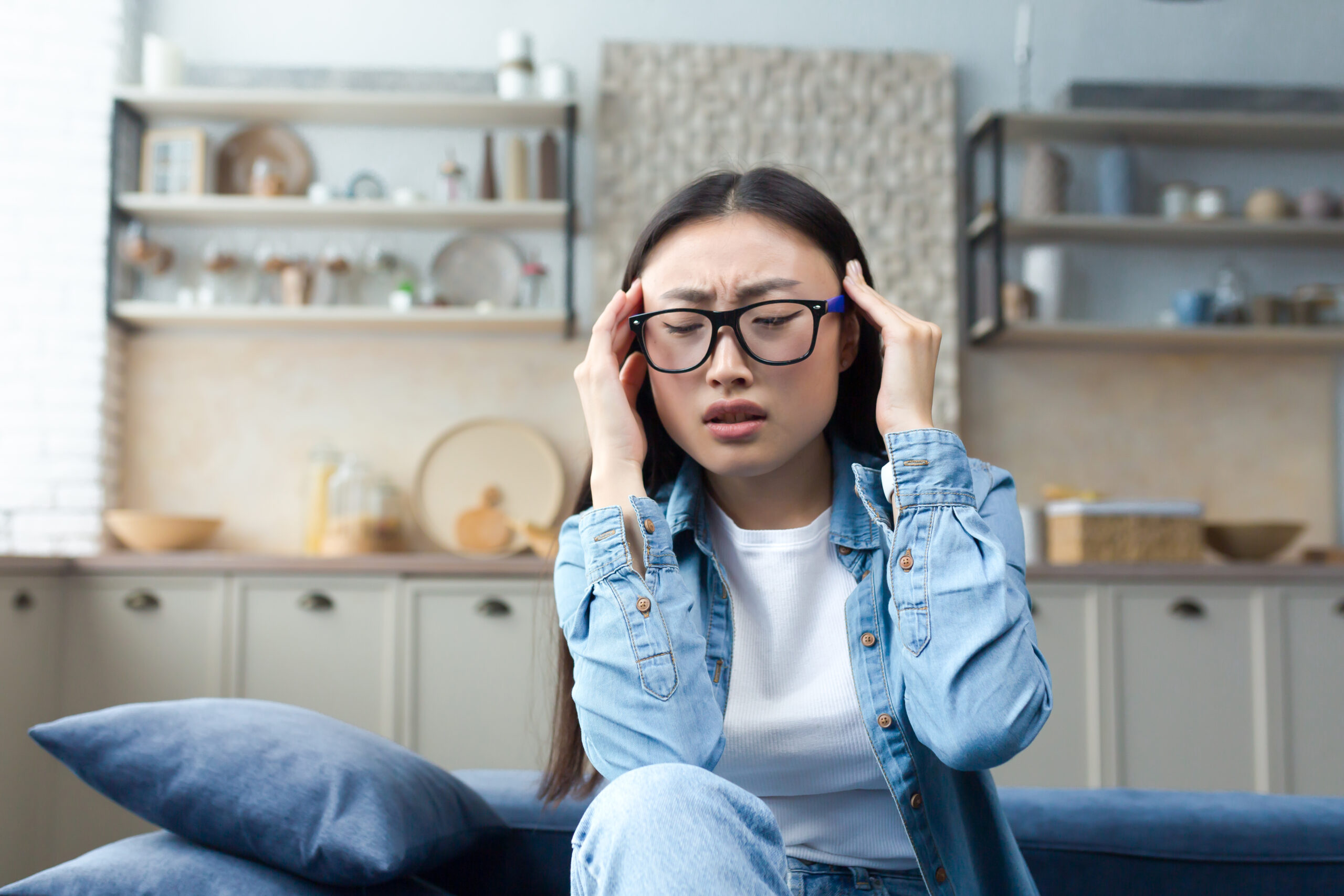 A young beautiful Asian woman holds her head, feels pain, pressure